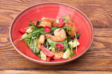 salad with shrimps, tomatoes and herbs in a plate on a wooden table