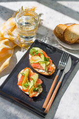 Open sandwiches with trout and cream cheese with cucumber on a dark plate - a tray on a gray table...