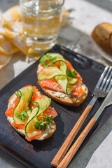 Open sandwiches with trout and cream cheese with cucumber on a dark plate - a tray on a gray table on a bright sunny day