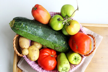 A full basket of seasonal vegetables. Zucchini, pepper, tomato, potatoes in a straw basket