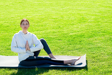 A woman practices yoga outdoors on the grass. Copy space