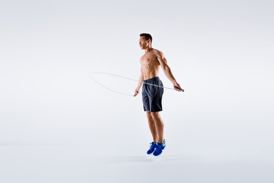 Full length photo of handsone sporty guy using skipping rope to train his perfect body isolated over white color background