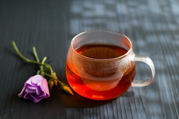 black tea in a transparent Cup next to a purple flower on a dark wooden background