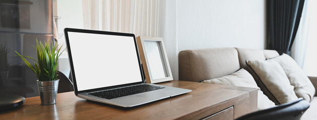 A white blank screen computer laptop is putting on a wooden table in a comfortable room.