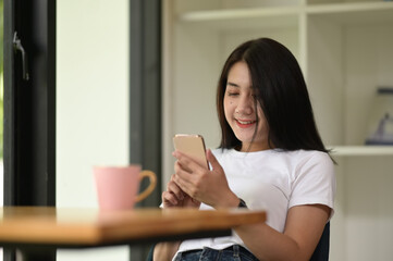 A beautiful woman is using a mobile phone while sitting at the wooden table.