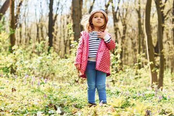Happy little girl in blue hat have walk in spring forest at daytime