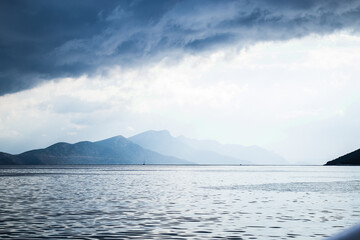 Dark clouds in the open sea. On the horizon are mountains on an island. Blue gradient. - 369698342