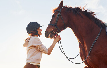 Young woman standing with her horse in agriculture field at sunny daytime