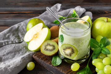 glass of yoghurt with fresh kiwi, green Apple, grapes and mint on a grey napkin