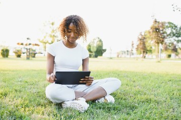 Online communication, education or work concept. Pretty African American lady with tablet computer at park