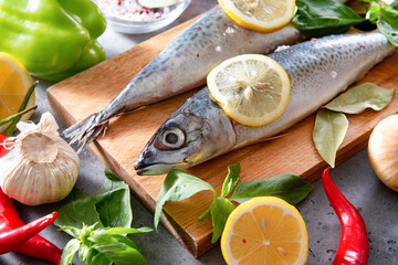 raw fish with lemon slices,  Basil, spices    knife, fork,  chili peppers, garlic  on the kitchen Board on a gray