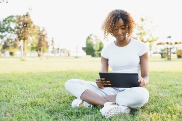 Cute black girl in a park. Lady in a white t-shirt and white jeans. Woman with tablet