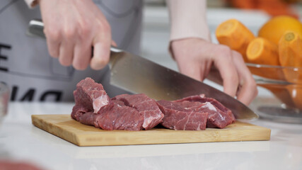 Woman cutting raw meat on small pieces with kitchen knife cutting board. Female cutting red beef filet on wooden board, holding knife in hand. Housewife is cooking at home interior. Concept: food
