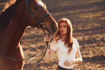 Obraz premium Young woman standing with her horse in agriculture field at sunny daytime