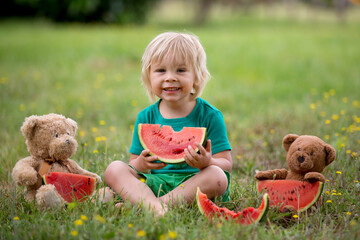 Cute little toddler child, blond boy, eating watermelon in the park