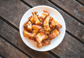 Fried pork rinds called “Torreznos” in a small white plate on a dark wooden table. Typical spanish snack to eat in a bar. 