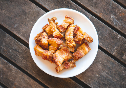 Fried pork rinds called &ldquo;Torreznos&rdquo; in a small white plate on a dark wooden table. Typical spanish snack to eat in a bar. 