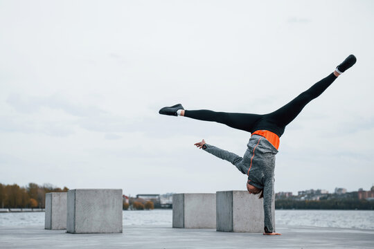 Young sportive girl doing parkour stunts outdoors near lake at daytime