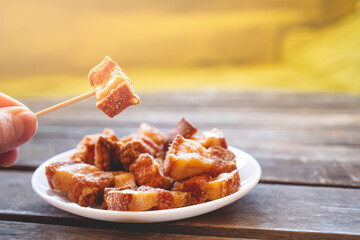 Hand holding a piece of fried pork rinds called “Torreznos” with a toothpick on a dark wooden table. Typicall spanish snacks to eat in a bar. Photo with selective focus. 
