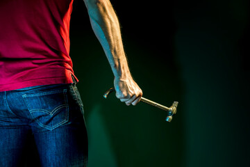 A male construction worker holds hammer in his  hand on a dark  background