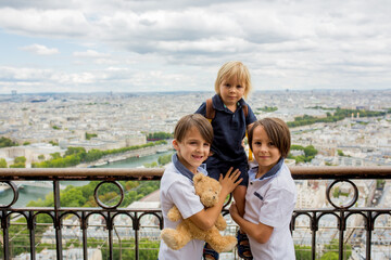 Happy children, boy brothers, holding teddy bear on top of the Eiffel tower, looking at the city, visiting Paris