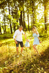 Fototapeta premium Young parents play with little daughter, smiling, caring dad and loving mom lift in air adorable baby girl, young family walking at the park, enjoy happy moments, weekend outdoors, childhood concept