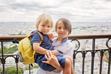 Fototapeta na wymiar Happy children, boy brothers, holding teddy bear on top of the Eiffel tower, looking at the city, visiting Paris