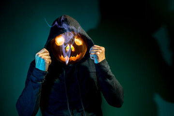A man with a glowing pumpkin instead of a head poses on a Halloween