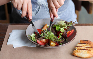 Woman eating healthy salad with beef, vegetables, herbs in cafe