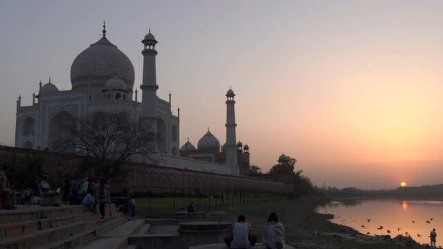 tourists watch the sunset behind the taj mahal and yamuna river in agra, india