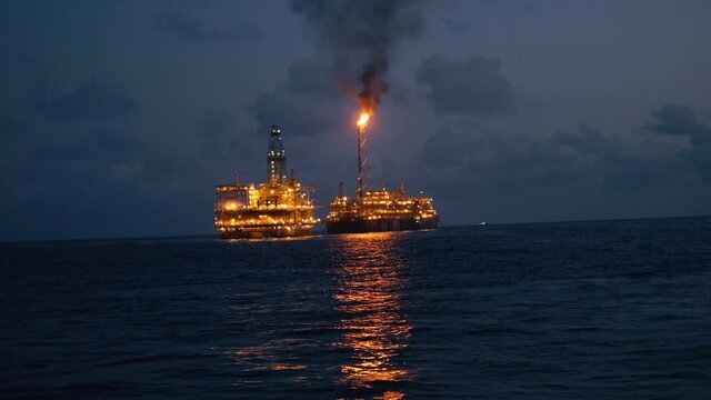 FPSO tanker vessel near Oil Rig platform. Offshore oil and gas industry. Flare is burning with smoke. Environmental pollution. 4k shot at night