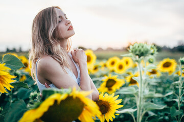 Obraz na płótnie Canvas Young, slender girl in a white T-shirt poses at sunset in a field of sunflowers