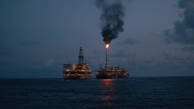 FPSO tanker vessel near Oil Rig platform. Offshore oil and gas industry. Flare is burning with smoke. Environmental pollution. 4k shot at night