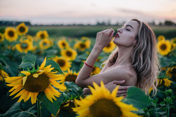 Young, slender girl topless poses at sunset in a field of sunflowers