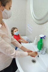 a woman and a child in medical masks wash their hands at the same time