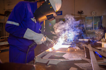 Welder is assembling the workpiece by process shielded metal arc welding (SMAW). Welder in blue...