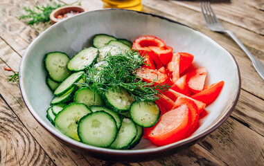Choped fresh tomato, cucumber for healthy vegetable salad. With dill, spices and olive oil in bowl on rustic wooden background.