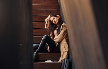 Fototapeta na wymiar Cheerful brunette in black leggings sitting on wooden stairs and smiling