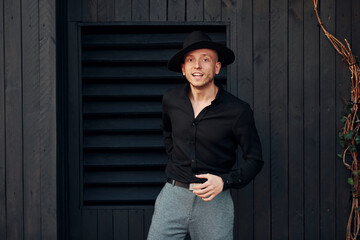 Man in black hat standing against black wooden building exterior