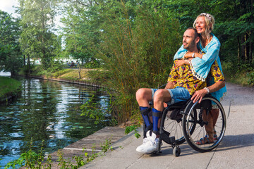 blond woman hugging man in wheelchair outdoors by river
