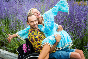 blond woman in blue dress sitting on lap of handsome man in wheelchair outdoors