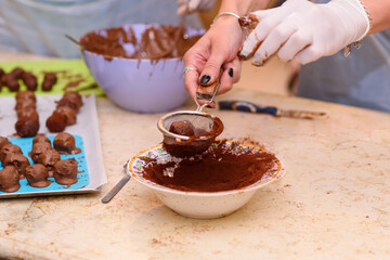 Cooking concept. Young woman making chocolate candies. Close up hands of a young girl preparing dessert, glazes a chocolate truffle with cocoa powder.