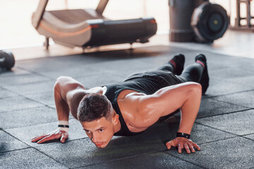 Doing push-ups. Young sportive strong man in black wear have workout day in gym