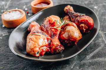 Chicken legs on black plate with red sauce and rosemary on black rustic background.