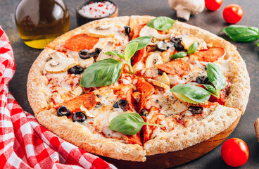 Sliced italian pizza with salami, mozzarella, mushroom, tomatoes, black olives and basil leaves on black background. Italian traditional food. Popular street food concept. Selective focus