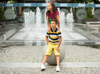 Two smiling kids, boy and girl playing together in town, city in summer day. Concept of childhood, happiness, sincere emotions, carefree lifestyle. Little caucasian models in bright clothes.