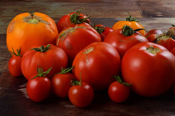 Abundance ripe organic tomatoes on dark rustic background. Colorful tomatoes 