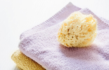 A natural yellow sponge on towels stacked on a white wooden table. Personal care and hygiene. Bath and relax