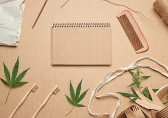 open notebook with empty sheets, a textile bag and disposable tableware from brown craft paper, green hemp leaves