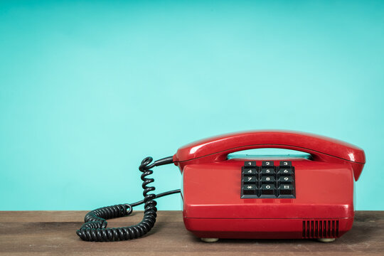 Old telephone on wooden table in front of green background. Vintage phone